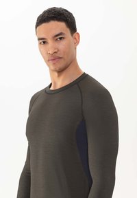 Chemise à manches longues vert olive foncé avec une coupe ajustée. Comprend un panneau contrastant bleu marine sur le côté et un tissu texturé.