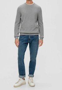 Graues strukturiertes Sweatshirt, blaue Jeans und weiße Turnschuhe. Das Outfit hat eine legere Passform und hochgekrempelte Jeansbündchen.