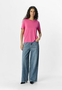 Pink short-sleeve top paired with wide-leg blue denim jeans, featuring a relaxed fit and smooth texture. Black pointed shoes complete the look.