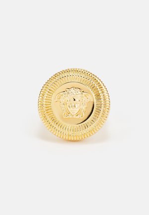 Bouton rond doré avec une tête de Méduse en relief détaillée au centre et une bordure texturée cannelée.