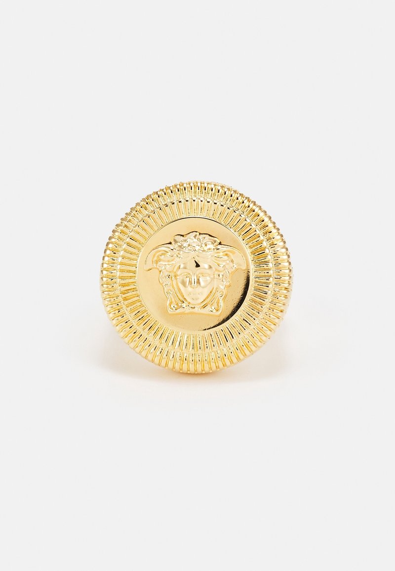 Bouton rond doré avec une tête de Méduse en relief détaillée au centre et une bordure texturée cannelée.