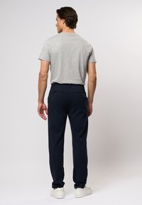 Szürke rövid ujjú pól�ó és sötétkék, slim fit nadrág sima anyagból, két hátsó zsebbel. Fehér sportcipők egészítik ki az öltözéket.