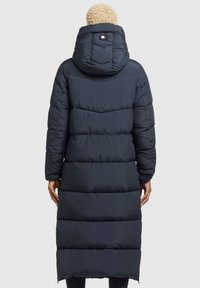 Marinblå pufferjacka med huva, med horisontella quiltade sektioner, en märkesknapp på baksidan och långa ärmar.