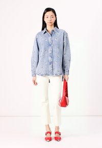 Ανοιχτό μπλε τζιν πουκάμισο με λουλουδάτη κεντημένη διακόσμηση, συνδυασμένο με λευκά cropped παντελόνια. Συνοδεύεται από μια κόκκινη τσάντα χειρός και κόκκινα μυτερά παπούτσια.