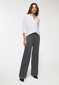 Camicia bianca con un leggero lucido, abbinata a pantaloni a palazzo a righe sottili grigio scuro e tacchi neri lucidi.