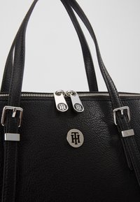 Bolso de mano de cuero negro con un acabado texturizado, herrajes de plata, cierre de doble cremallera y un acento de logo redondo en la parte frontal.