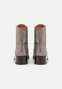 Para metalicznych taupe zamszowych botków za kostkę z ciemnymi, warstwowymi obcasami, pokazanych z tyłu na białym tle.