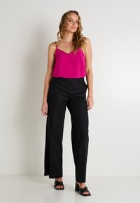 Camisole en satin fuchsia avec bordure en dentelle associé à un pantalon large taille haute noir et des sandales à talons noirs. Texture lisse, coupe décontractée.