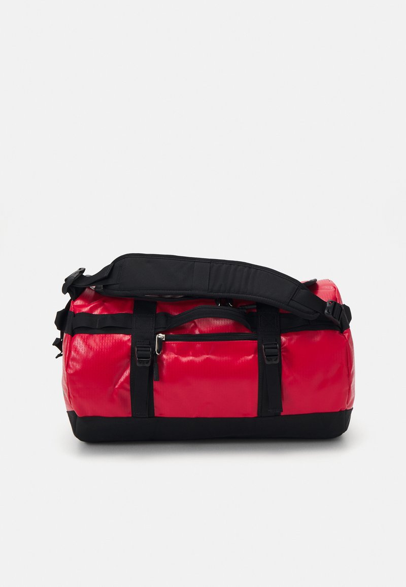Red duffel bag with a glossy finish, black straps and base, featuring a zippered pocket and adjustable shoulder strap. Sturdy design.