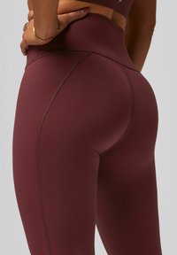 Hochgeschnittene Athleisure-Leggings in dunklem Burgunderrot. Glattes, elastisches Material mit tonalem Nähen, entworfen für Komfort und Unterstützung.