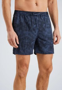 Shorts de bain navy avec un motif texturé, taille élastique et cordon de serrage ajustable. Longueur mi-cuisse. Le matériau semble léger et durable.