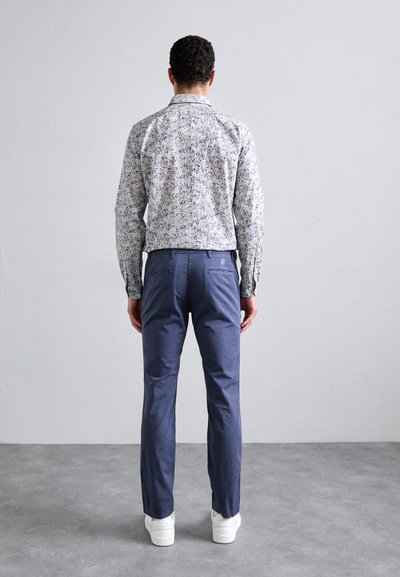 Camicia a maniche lunghe da uomo con motivo floreale, abbinata a pantaloni blu navy. La camicia presenta uno sfondo chiaro e dettagli sottili.