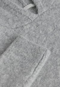 Šedý fleecový svetr s měkkou texturou, se stojáčkem a štítkem s nápisem "NEXT". Jemné variace v barvě a tloušťce.