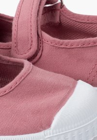 Zapatilla de lona rosa con parte superior texturizada, puntera de goma blanca y tira de Velcro. Presenta costuras reforzadas y una suela flexible.