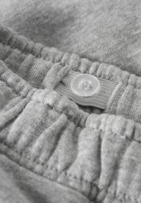 Siv pas elastik s satenom teksturo, ki vključuje prozoren plastičen gumb in tekstilno zanko za varno zapiranje.