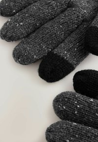 Stickade vantar i varierande nyanser av grått, med ett strukturerat mönster och kontrasterande svarta fingertoppar. Mjuk ullblandning.