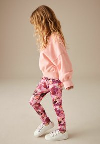 Felpa rosa oversize abbinata a leggings floreali colorati nelle tonalità di rosa e viola; completata da sneakers bianche con cinture glitterate.