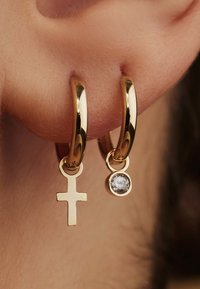 Gold hoop earrings featuring a cross and a clear gemstone pendant. Smooth, reflective surface; small, circular design with a dangling accent.