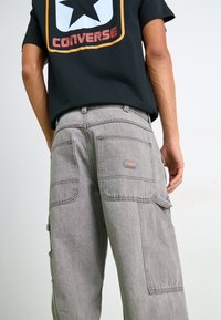 Gray cargo pants with multiple pockets, sturdy fabric, straight leg design, and visible stitching details, paired with a black graphic T-shirt.
