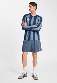 Sportkläder med en långärmad tröja i marinblå och ljusblå ränder med v-ringning och logotyp, i kombination med andningsbara mesh-shorts.