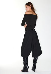 Schwarzes, schulterfreies Oberteil kombiniert mit schwarzen, weit geschnittenen Hosen mit einem mit Nieten besetzten Taille und glänzenden kniehohen Keilstiefeln.