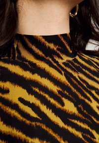 Tigerprint-Oberteil mit hohem Kragen. Verfügt über kräftige Schwarz- und Goldgelb-Töne, eine glatte Textur und ein körperbetontes Design.
