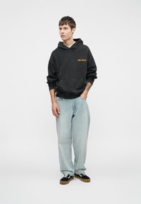 Czarna bluza z kapturem z przednią kieszenią, z złotym napisem. Jasnoniebieskie luźne dżinsy, czarne tenisówki z białymi akcentami. Prosty i casualowy design.