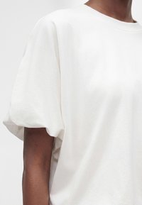 Gros plan d'une personne portant une chemise blanche ample à manches courtes bouffantes avec un col rond.