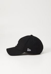 Sort baseball cap med rund krone, flad skygge og broderet hvidt logo på fronten. Har ventilationshuller og et emblem på siden.
