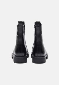 Botas de cuero negras hasta el tobillo con un acabado texturizado, cierre de cremallera y suelas de goma resistentes, que presentan un diseño elegante y aerodinámico.