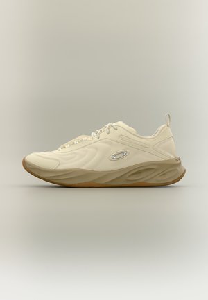 Kremowy sportowy sneaker z teksturowanymi bokami, grubą brązową podeszwą, sznurowadłami i małym owalnym logo z boku, pokazany z profilu na jednolitym tle.