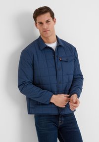 Navy blue quilted jacket with button closure and a chest pocket detail. Made from lightweight material, featuring long sleeves and a collar.