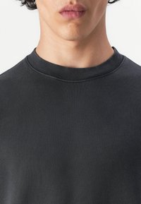 Svart crewneck sweatshirt med ribbet krage og teksturert stoff. Designet er minimalistisk uten synlige logoer eller mønstre.