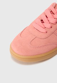 Suede rosa sneakers med rund tå, platta snörningar och gummisula. Har stickade detaljer och en texturerad ovandel.