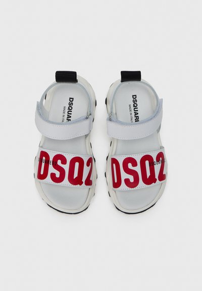 Sandales blanches avec une semelle épaisse noire, dotées d'une large bande rouge avec l'inscription "DSQUARED2". Bride réglable en gris clair. Design plat et ouvert.