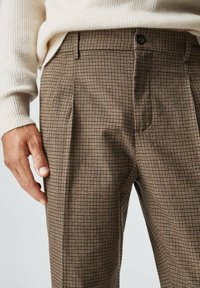 Ruske ručno provjerene hlače s nabranima, s kopčanjem na dugme. Mekana tekstura s suptilnim dezenom, upotrebljene uz svijetlu pletenu majicu.