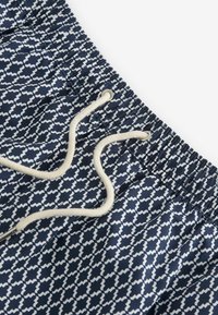 Costume da bagno blu navy con un motivo geometrico bianco, caratterizzato da una vita elastica e un cordoncino, realizzato in tessuto leggero.