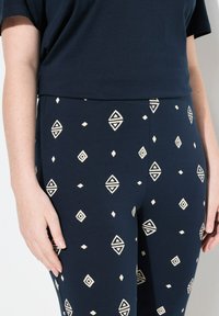 Granatowe legginsy wykonane z miękkiego materiału z kremowymi geometrycznymi wzorami, w tym diamentami i trójkątami, z elastycznym pasem.