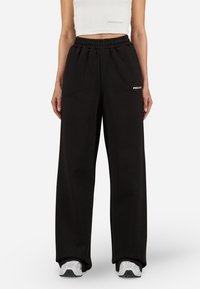 Black, wide-leg sweatpants with an elastic waistband, featuring a small white logo on the side. Made from soft fabric with a smooth texture.