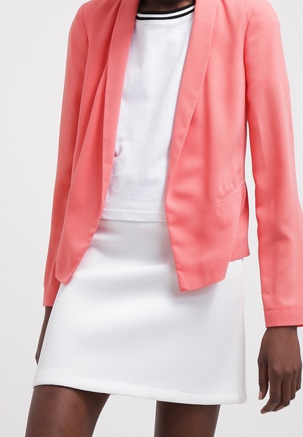 Blazer corallo con una vestibilità su misura, indossato su una maglietta a rete bianca, abbinato a una minigonna bianca con una texture liscia e un delicato dettaglio all'orlo.