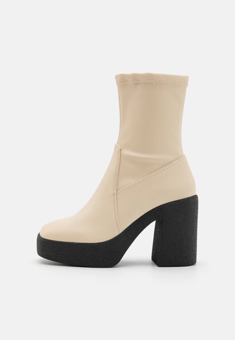 Botte beige mi-mollet avec tige souple, bout arrondi, talon bloc noir épais texturé et semelle plateforme.