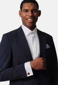 Navy suit jacket with a white dress shirt and patterned pocket square. Cufflinks feature a round design with an intricate accent.