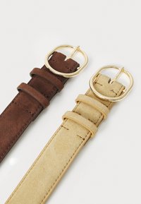 Deux bracelets de montre en daim, l'un marron et l'autre beige. Chacun présente une boucle dorée et des anses de maintien. Un détail de surface texturée est visible.