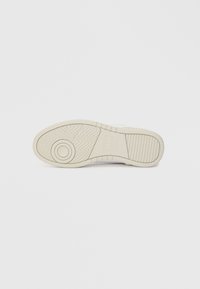 Σόλα λευκού αθλητικού παπουτσιού με κυκλικό σχέδιο πέλματος και ορθογώνιο λογότυπο στο κέντρο, σε λευκό φόντο.