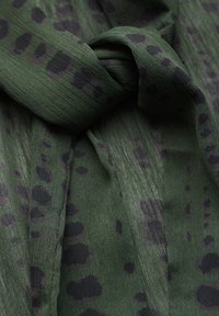 Sciarpa di stoffa verde con un motivo testurizzato caratterizzato da macchie circolari nere. Il materiale sembra leggero e leggermente trasparente.