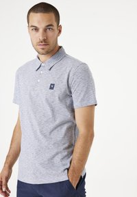 Camisa polo de rayas grises con collar, que presenta un pequeño logo en navy en el pecho. Mangas cortas y un corte relajado. Textura suave.
