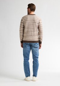 Braun und beige gestreifter Pullover mit Rundhalsausschnitt und gerippten Bündchen, kombiniert mit hellblauen Jeans und weißen Sneakers.