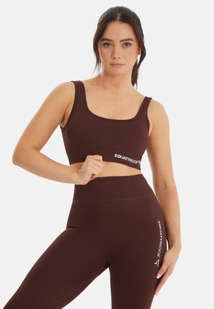 Dark brown ribbed sports bra and matching leggings with "SQUATPROOF" logo. Square neckline, wide straps, high waist design, smooth texture.