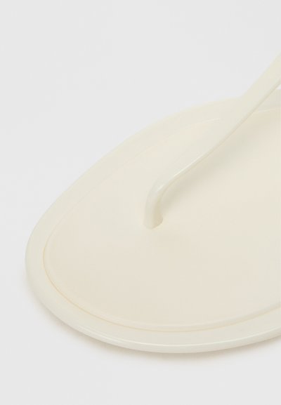 Cream-colored flip-flop with a smooth, rounded sole and a thin, curved strap. The design is minimalistic with no visible patterns or accents.