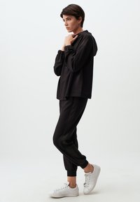 Zwarte hoodie met een verstelbare trekkoord en elastische manchetten, gecombineerd met bijpassende joggers met een tapse lijn. Draagt met witte sneakers.